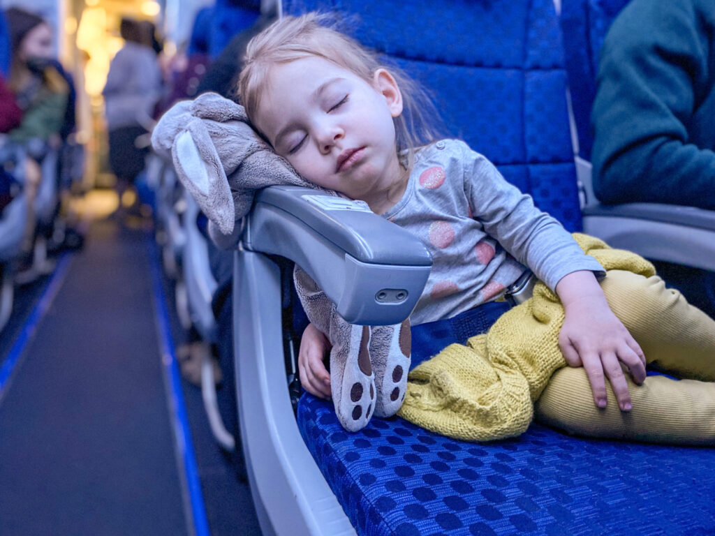 a toddler girl sleeping on an airplane