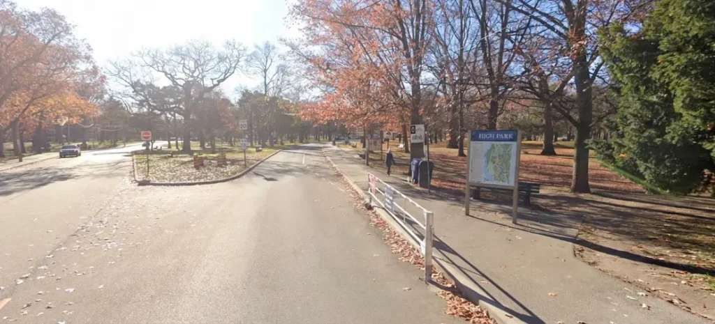 High Park Toronto entrance on West Road with park map sign, autumn trees, fallen leaves, and pedestrian walkway in sunny fall setting