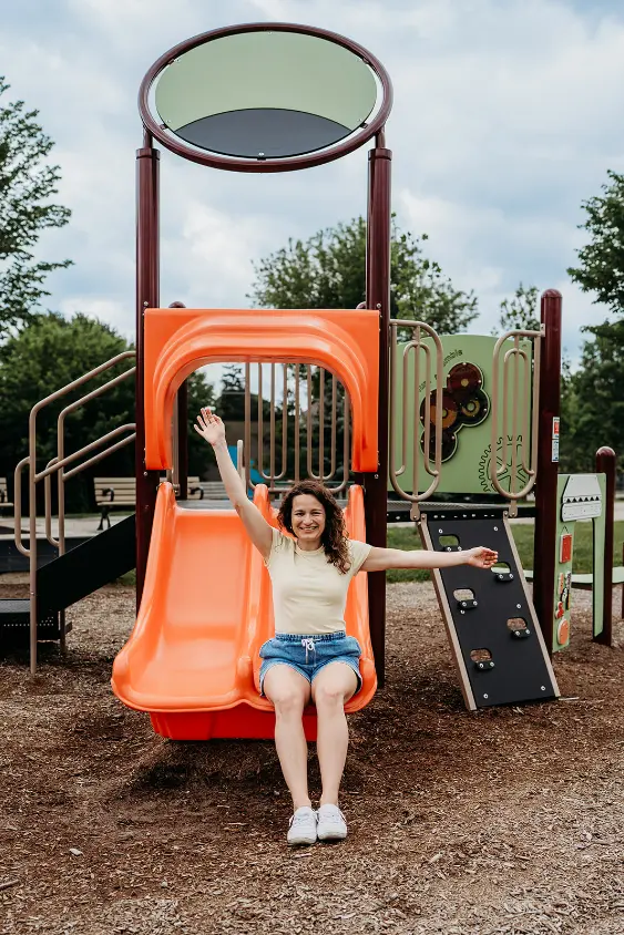 Nicole Kingsotn sitting on a slide in a playground in Toronto with her one hand in the air and the other stetched out at her shoulder